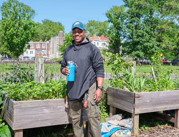 photo of Michael, armed with a reusable bottle full of refreshing Philly tap water, standing in his community garden, with Philly rowhomes in the background